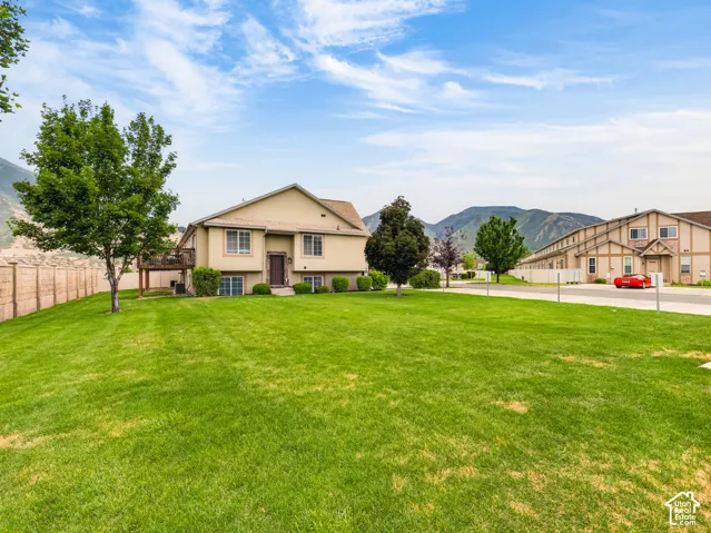 Expansive backyard featuring a large grass lawn, mature trees, wood-fencing, and a raised wooden deck, set against a mountain backdrop