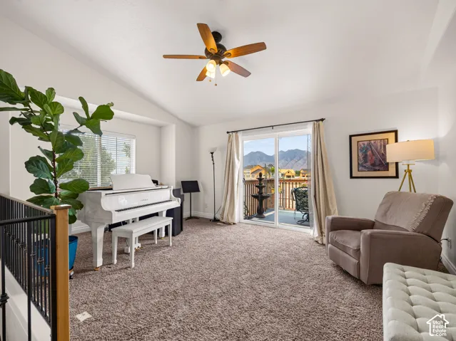 Vaulted ceilings featuring a central ceiling fan with integrated lighting, carpeted flooring, and sliding glass doors opening to an exterior balcony with mountain scenery