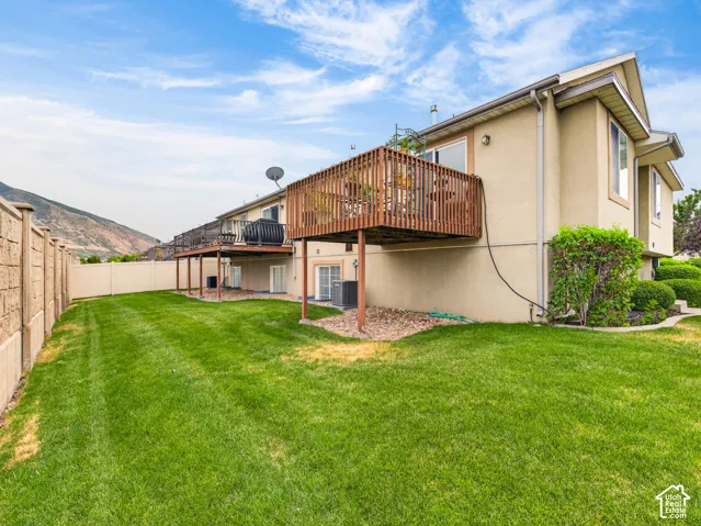 Rear exterior featuring an elevated wood deck, stucco siding, a fenced yard, and mountain scenery