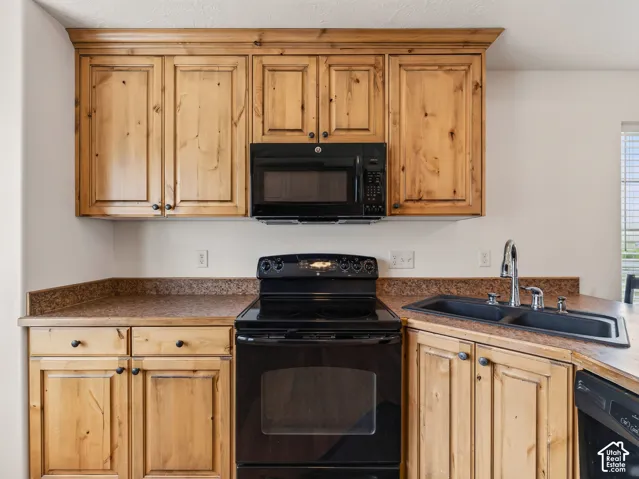Knotty pine cabinetry with crown molding, integrated black appliances, stone-composite countertops, and a dual-basin sink with a gooseneck faucet