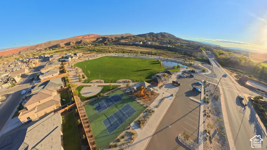 Aerial perspective featuring a large grass park, tennis courts, a pond, and desert mountain backdrop