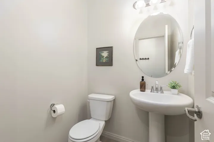 Oval wall-mounted mirror, pedestal sink with chrome faucet, and three-light vanity fixture