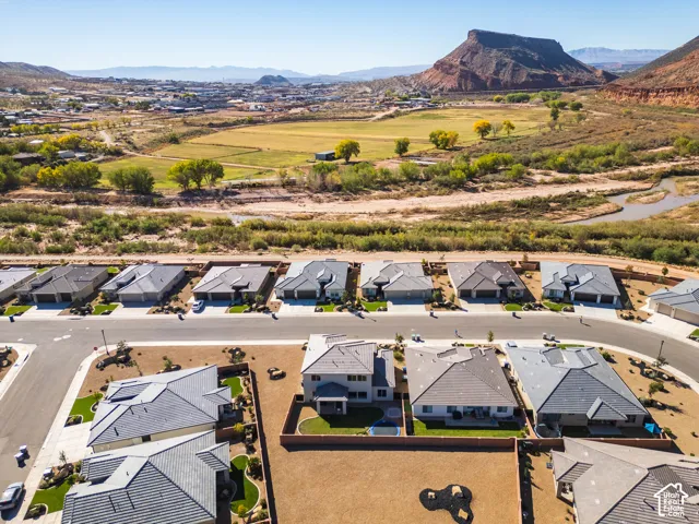 Aerial perspective of a residential development featuring single-story homes with composition shingle roofs, paved streets, concrete driveways, and expansive natural desert landscapes set against mountain scenery