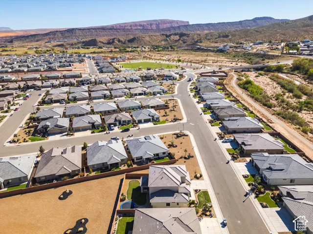 Aerial perspective of a residential neighborhood featuring paved streets, single-story residences with pitched roofing, manicured lawn areas, and prominent mountain backdrops