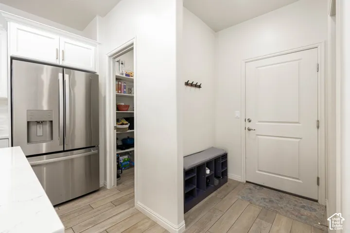 Stainless steel French-door refrigerator, walk-in pantry with built-in shelving, wood-finish flooring, and solid-core paneled door