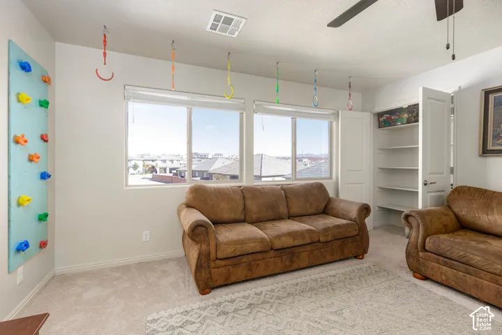 Room featuring neutral wall-to-wall carpeting, dual windows with blinds, ceiling fan, and built-in closet shelving