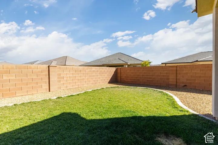 Rear yard featuring a sod lawn, concrete edging, gravel ground cover, and masonry perimeter wall