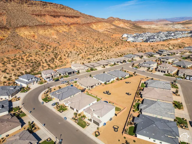 Aerial perspective featuring residential lots with desert landscaping, paved streets, and a prominent sandstone mountain backdrop