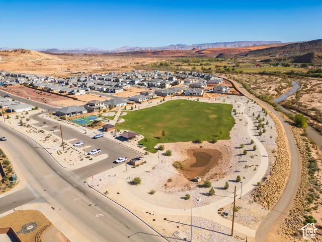 Aerial perspective of community grounds featuring a central manicured lawn, paved walking paths, a multi-sport court, and desert-toned mountain terrain