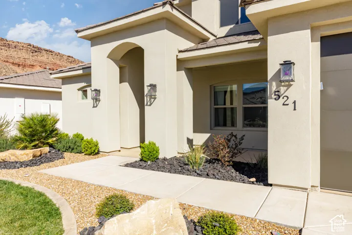 Stucco exterior featuring an arched entry, decorative wall-mounted lanterns, concrete walkway, desert-inspired landscaping, and a mountain backdrop