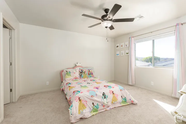 Neutral-toned interior space featuring light-colored wall-to-wall carpeting, a multi-blade ceiling fan with integrated lighting, and a single-pane sliding window