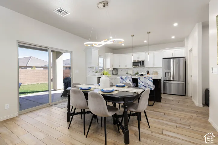 Kitchen featuring white cabinetry, stainless steel appliances, a center island with pendant lighting, and wood-finish tile flooring throughout the area