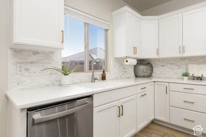 Kitchen featuring white shaker-style cabinetry, solid-surface countertops, multi-tonal stacked stone backsplash, stainless steel dishwasher, and an undermount sink with a gooseneck faucet