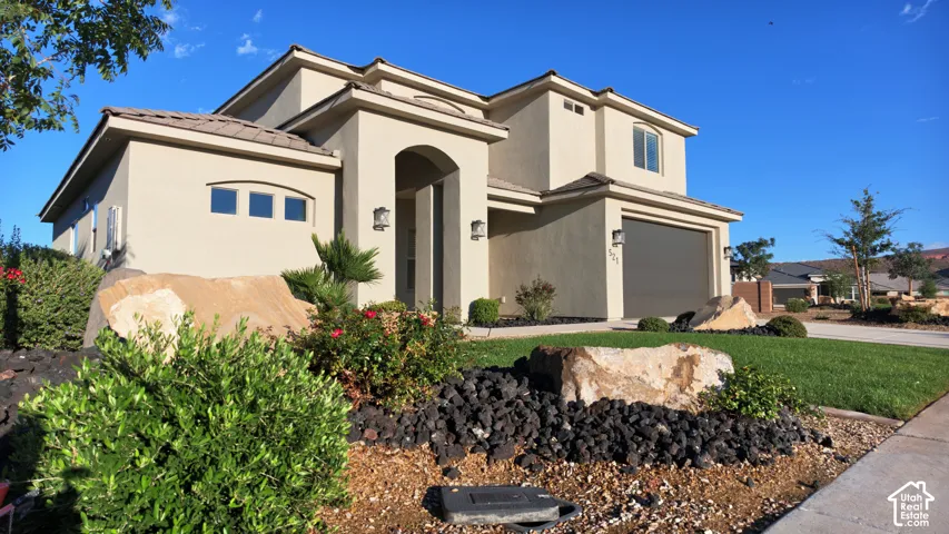 Stucco exterior featuring an arched entry, multi-level roofline, attached garage, and manicured landscaping with decorative rock accents