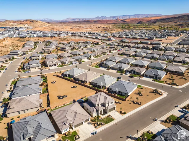 Aerial perspective of a residential development featuring expansive desert topography, paved streets, and a prominent mountain backdrop