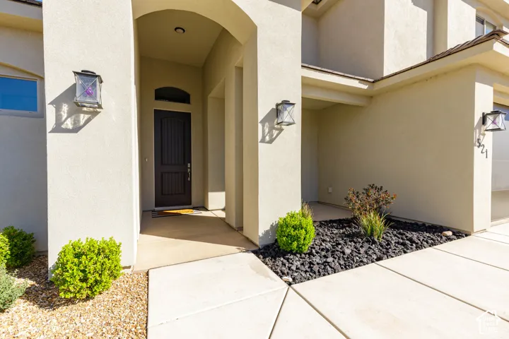 Stucco exterior featuring a recessed entryway, dark-finished entry door with an arched transom window, wall-mounted exterior lanterns, and low-maintenance rock landscaping