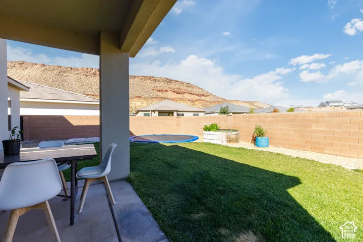 Covered concrete patio with a landscaped lawn and perimeter block wall, featuring a backdrop of desert mountain terrain