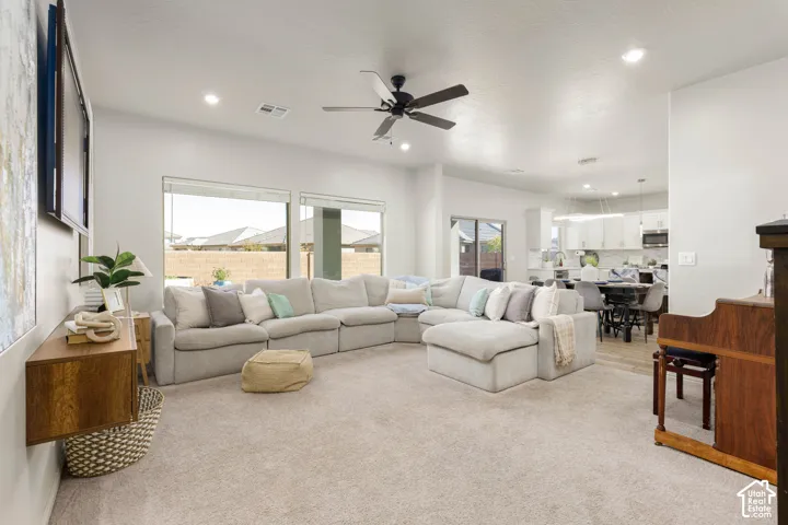 Open-concept living space featuring high ceilings, recessed lighting, a matte black ceiling fan, expansive windows, and wall-mounted wooden cabinetry