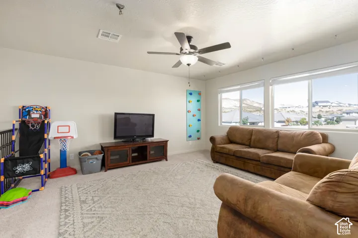 Neutral-toned interior featuring carpeting, a ceiling fan with integrated lighting, dual large windows, and a wall-mounted climbing panel