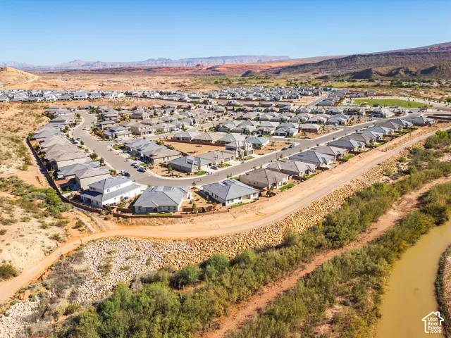 Aerial perspective of a residential development featuring single-story dwellings, paved thoroughfares, desert landscape, and mountainous horizon