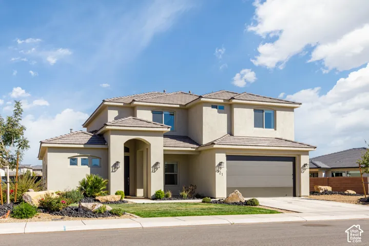 Stucco exterior featuring an arched entryway, tile roof, multi-level architectural design, and an attached two-car garage