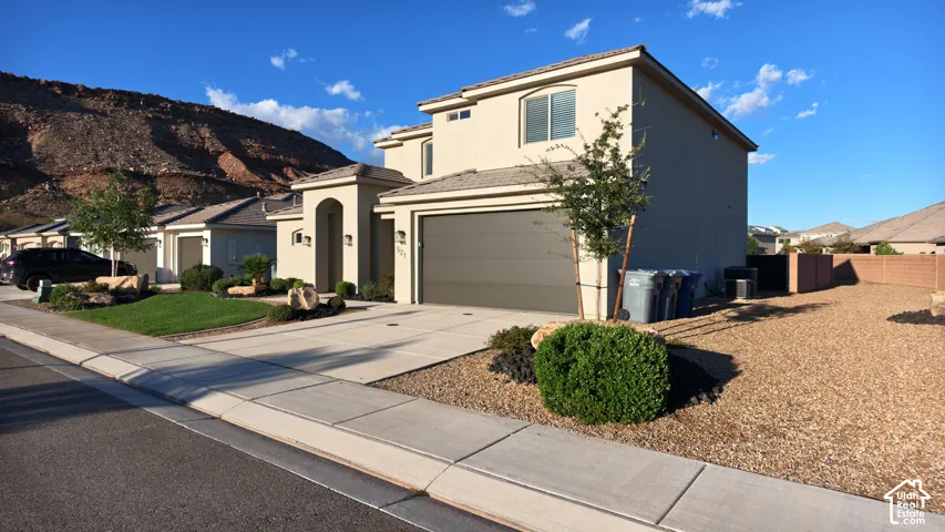 Modern two-story residence featuring a sleek gray exterior with clean architectural lines, wide driveway with concrete pavement, low-maintenance xeriscaped front landscaping with decorative rock and shrub plantings, two-car garage with paneled door, and m
