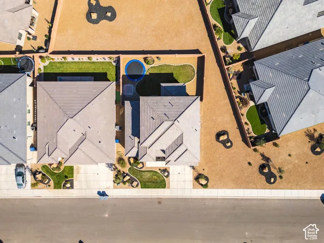 Aerial perspective of residential property featuring a concrete driveway, multi-faceted roofline, walled perimeter, and landscaped lawn