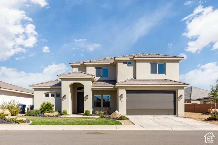 Stucco exterior residence featuring a multi-level roofline, arched covered entryway, integrated two-car garage, and desert-inspired landscape design
