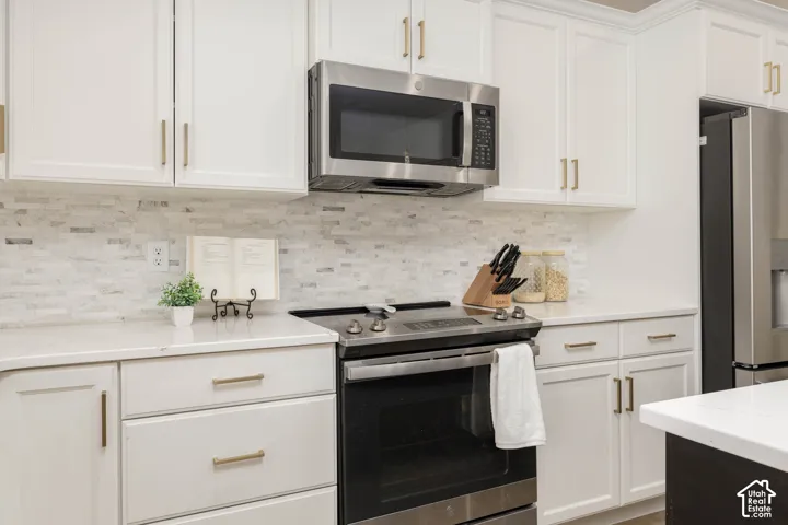Kitchen featuring white shaker-style cabinetry, quartz countertops, a stone mosaic tile backsplash, and stainless steel appliances including an over-the-range microwave and electric range