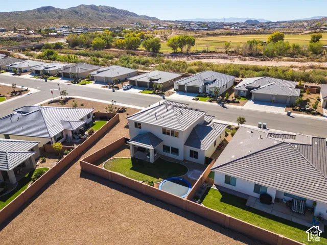 Two-story residence featuring a tile roof, covered rear patio, enclosed backyard with a grass lawn, and desert mountain backdrop