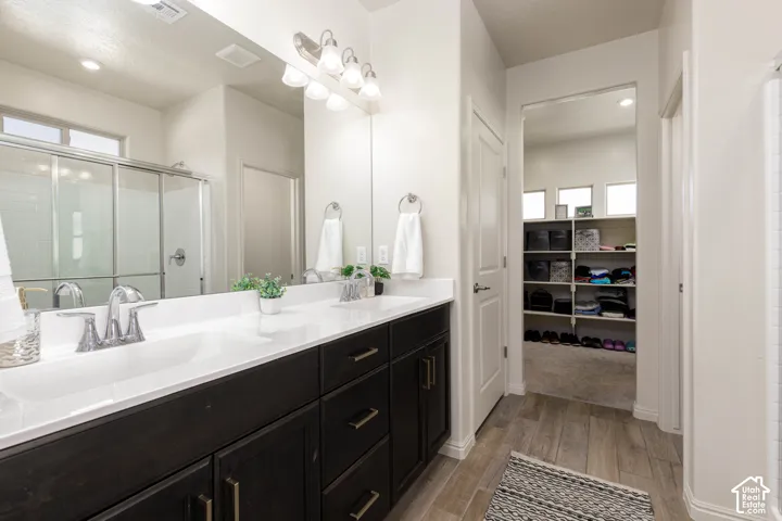 Dual-sink vanity with a solid-surface countertop, dark-finish cabinetry, full-width mirror, and walk-in storage area featuring built-in shelving