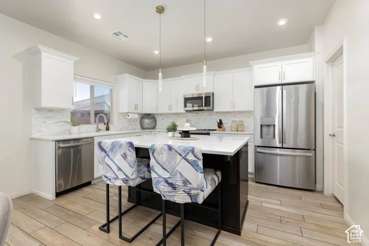 Kitchen featuring white cabinetry, an oversized central island with stone-surface countertop, stainless steel appliances, tile backsplash, and wood-finish flooring