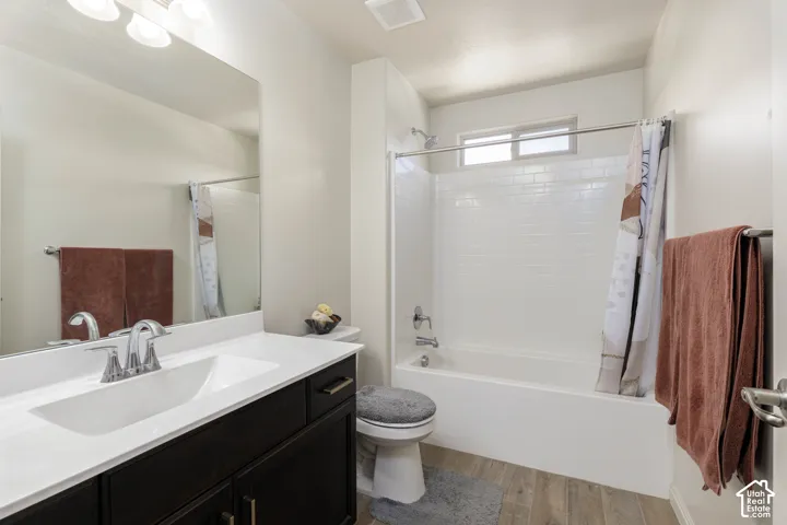 Bathroom featuring a dark wood-finish vanity with a white countertop, large wall-mounted mirror, wood-finish flooring, and a tub-shower combination with white subway-style tile surround