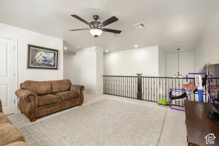 Open loft space featuring neutral carpeting, a dark metal balustrade, and a multi-blade ceiling fan with integrated lighting
