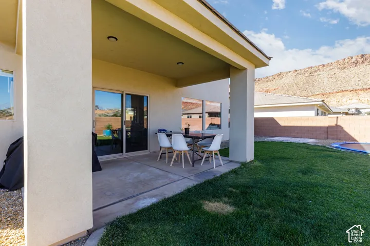 Covered concrete patio featuring recessed lighting, sliding glass door, grass lawn, and stone masonry perimeter wall with a mountain backdrop