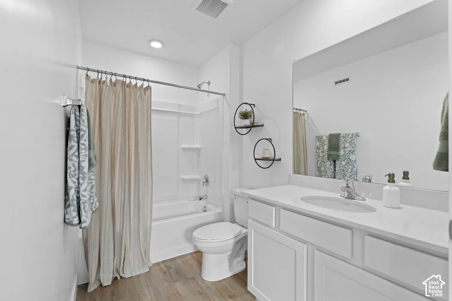 Bathroom featuring a white vanity with a solid surface countertop, an oval undermount sink, a full-width mirror, wood-finish flooring, and a tub-shower combination with a surround unit
