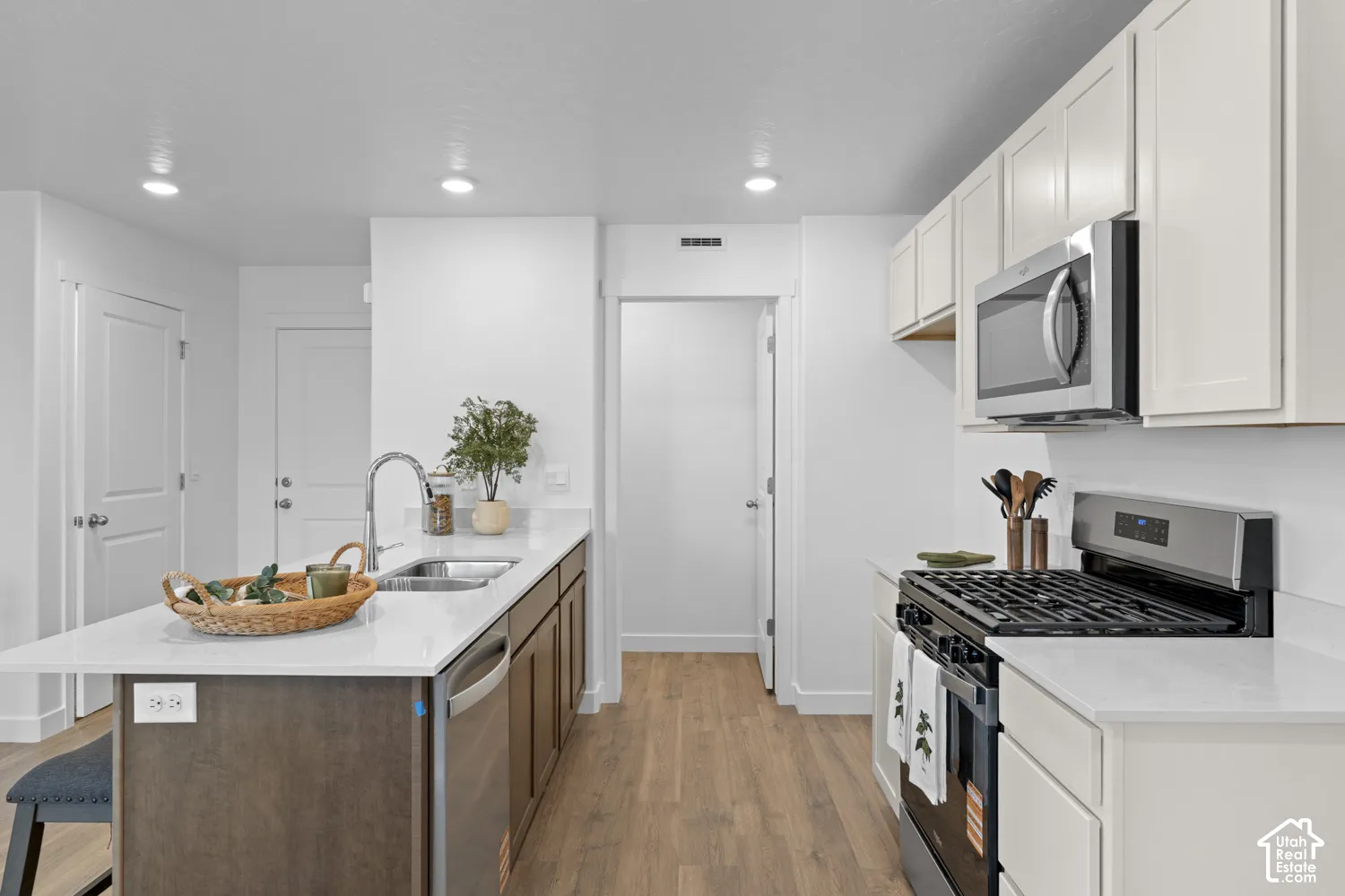 Kitchen featuring white cabinetry, solid-surface countertops, stainless steel gas range, built-in microwave, and wood-finish flooring