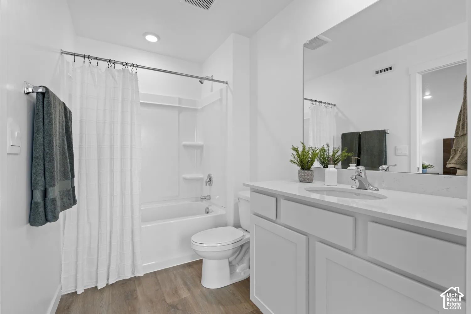 Bathroom featuring wood-finish flooring, a white vanity with a composite countertop, an undermount oval sink, and a combination bathtub and shower with a white surround