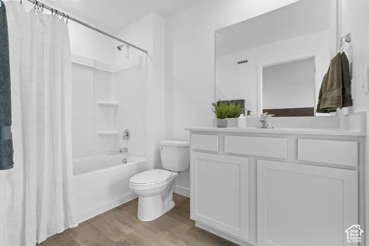 Bathroom featuring a white vanity with a rectangular countertop, large wall-mounted mirror, wood-finish flooring, and a shower-tub combination with integrated shelving