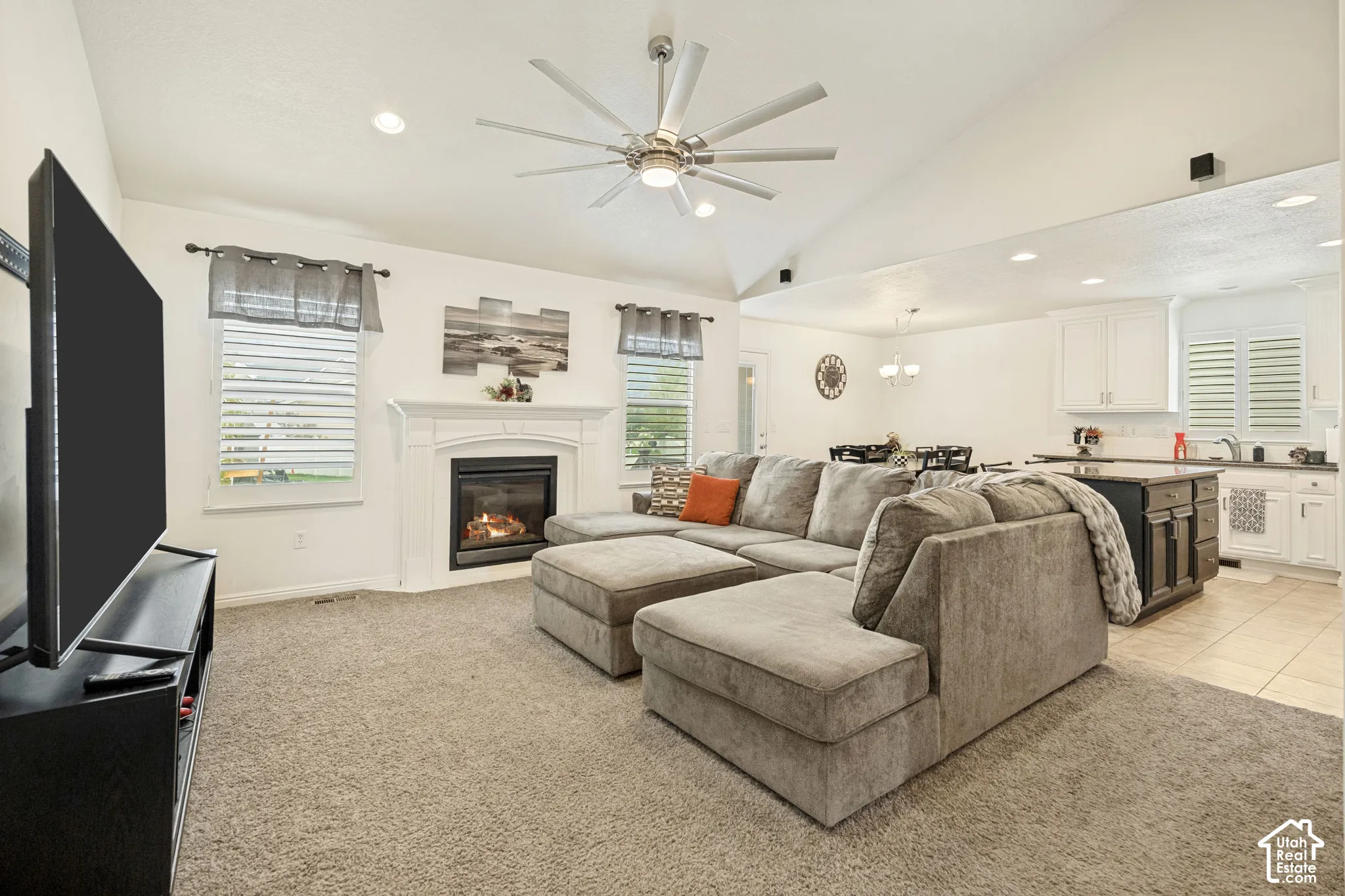 Vaulted ceilings featuring a multi-blade ceiling fan, inset lighting, a fireplace with a white mantel, and plantation shutters