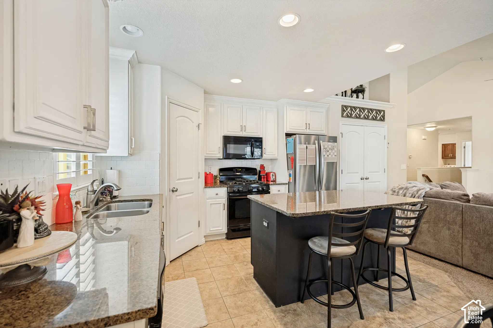 Kitchen featuring white cabinetry, stone-finish countertops, stainless steel appliances, a center island with a dark finish, and tile flooring
