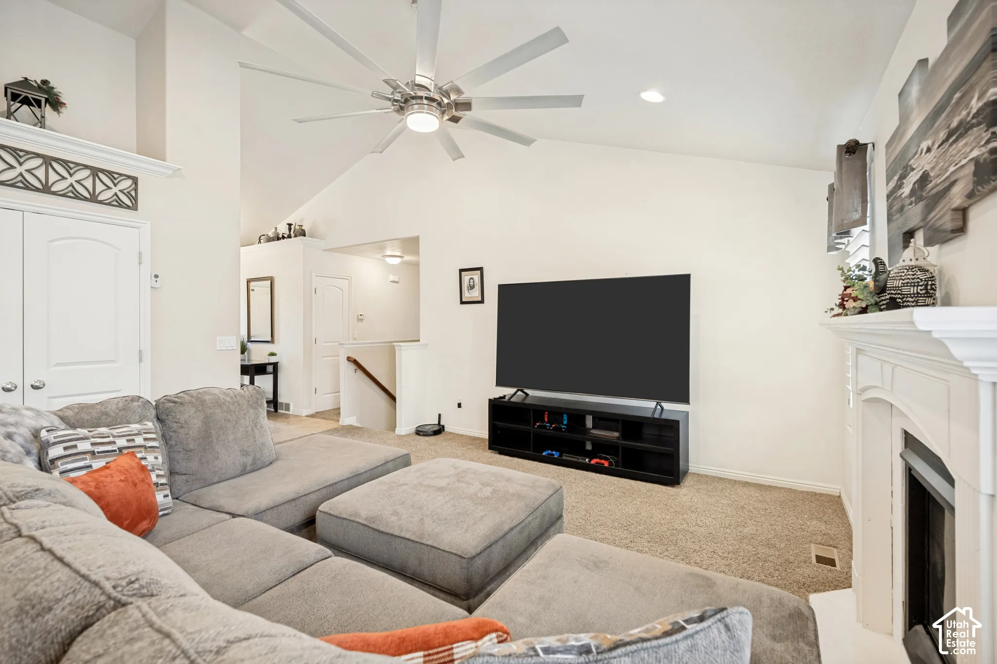 Vaulted ceiling featuring a central multi-blade ceiling fan, arched fireplace mantel with decorative molding, and double-door entry