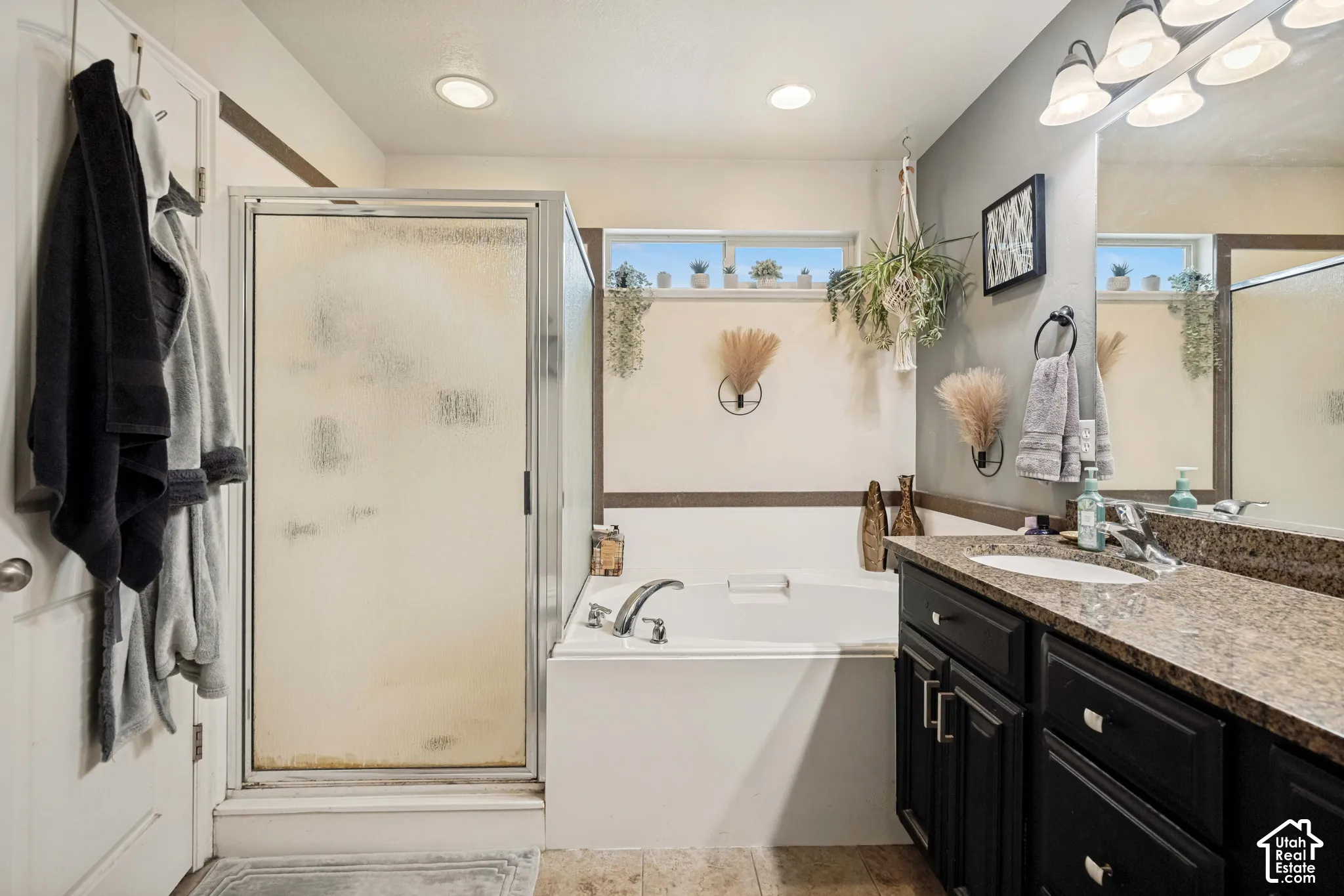 Bathroom featuring a soaking tub, glass-enclosed shower, dark-finished cabinetry, stone-surface countertop, and an integrated oval sink