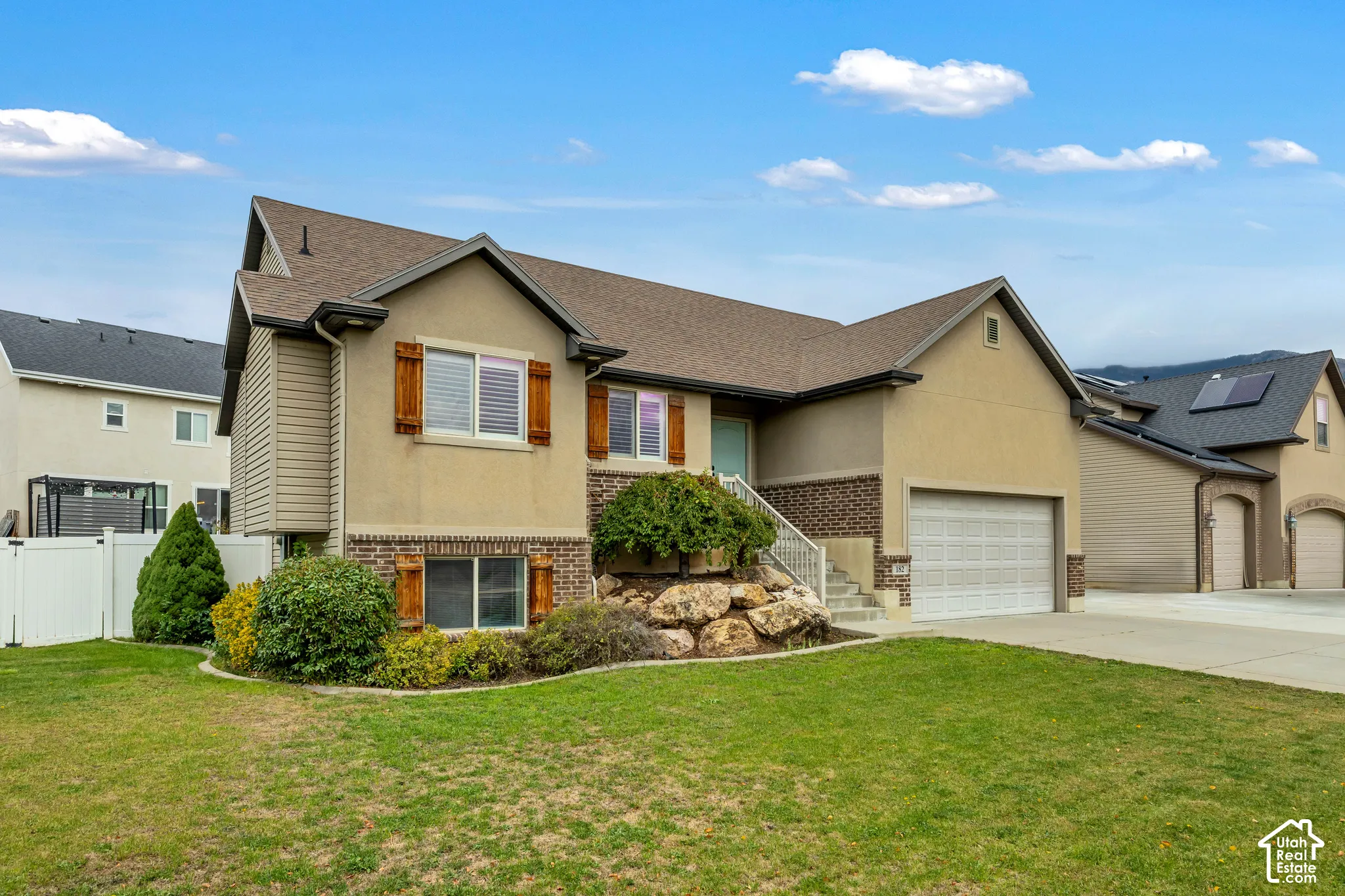 Exterior featuring a stucco and brick facade, attached two-car garage, decorative wood-finish shutters, and landscaped garden with stone boulders