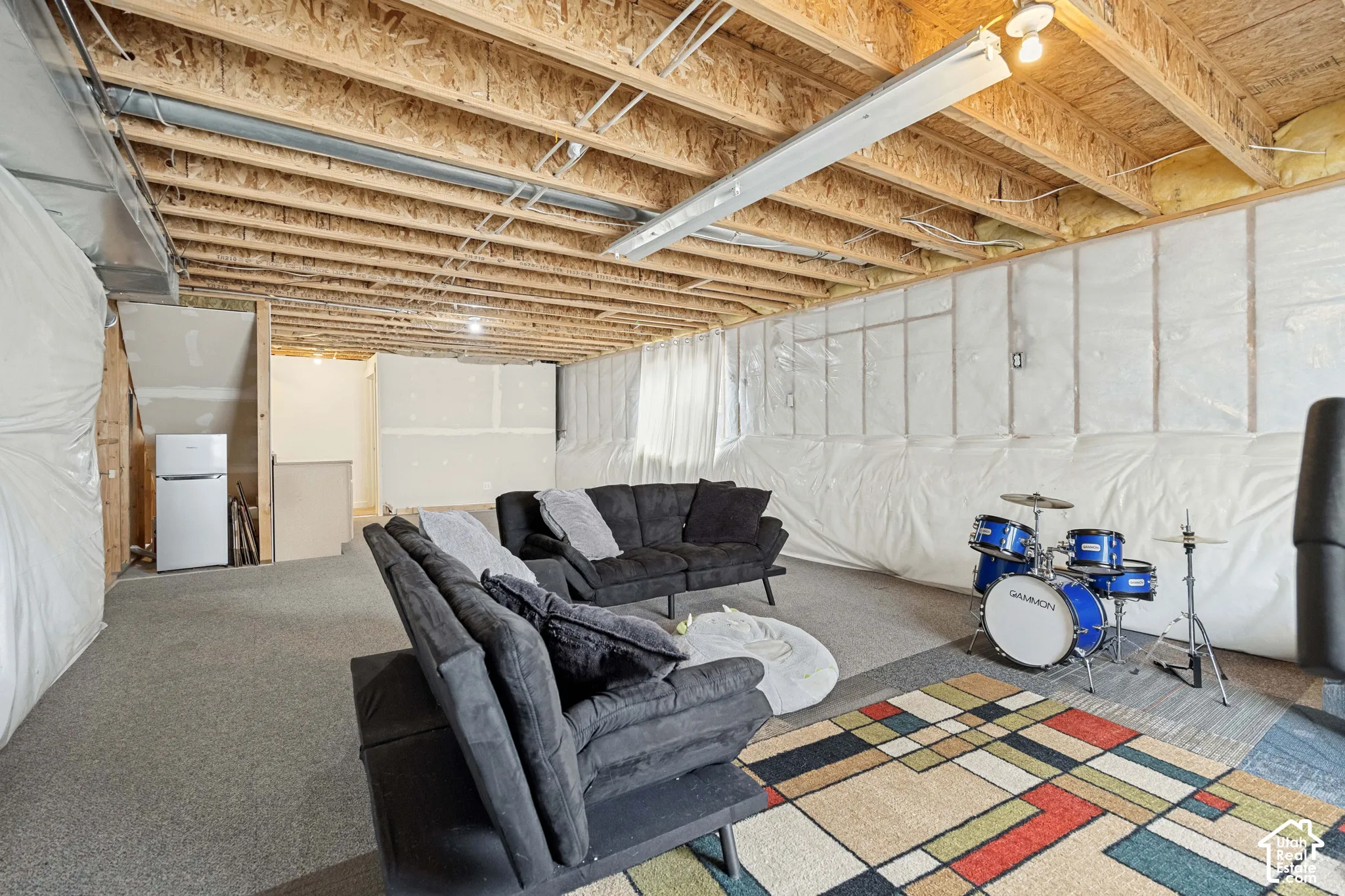 Unfinished lower level featuring exposed wood joist ceilings, wall vapor barriers, and wall-to-wall carpeting