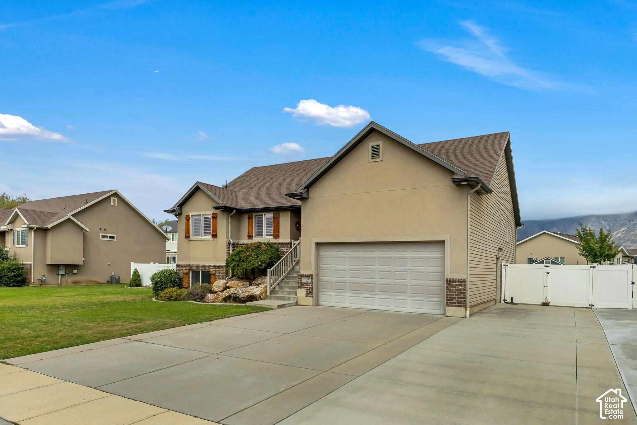 Multi-level exterior featuring a stucco and siding facade, attached two-car garage, concrete driveway, rock landscaping, and a vinyl perimeter fence