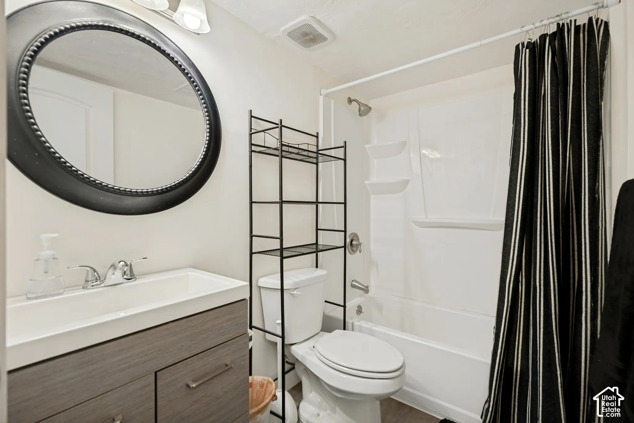 Wood-finish vanity cabinet, white integrated sink with dual-handle faucet, oval wall-mounted mirror, and white combination tub and shower surround
