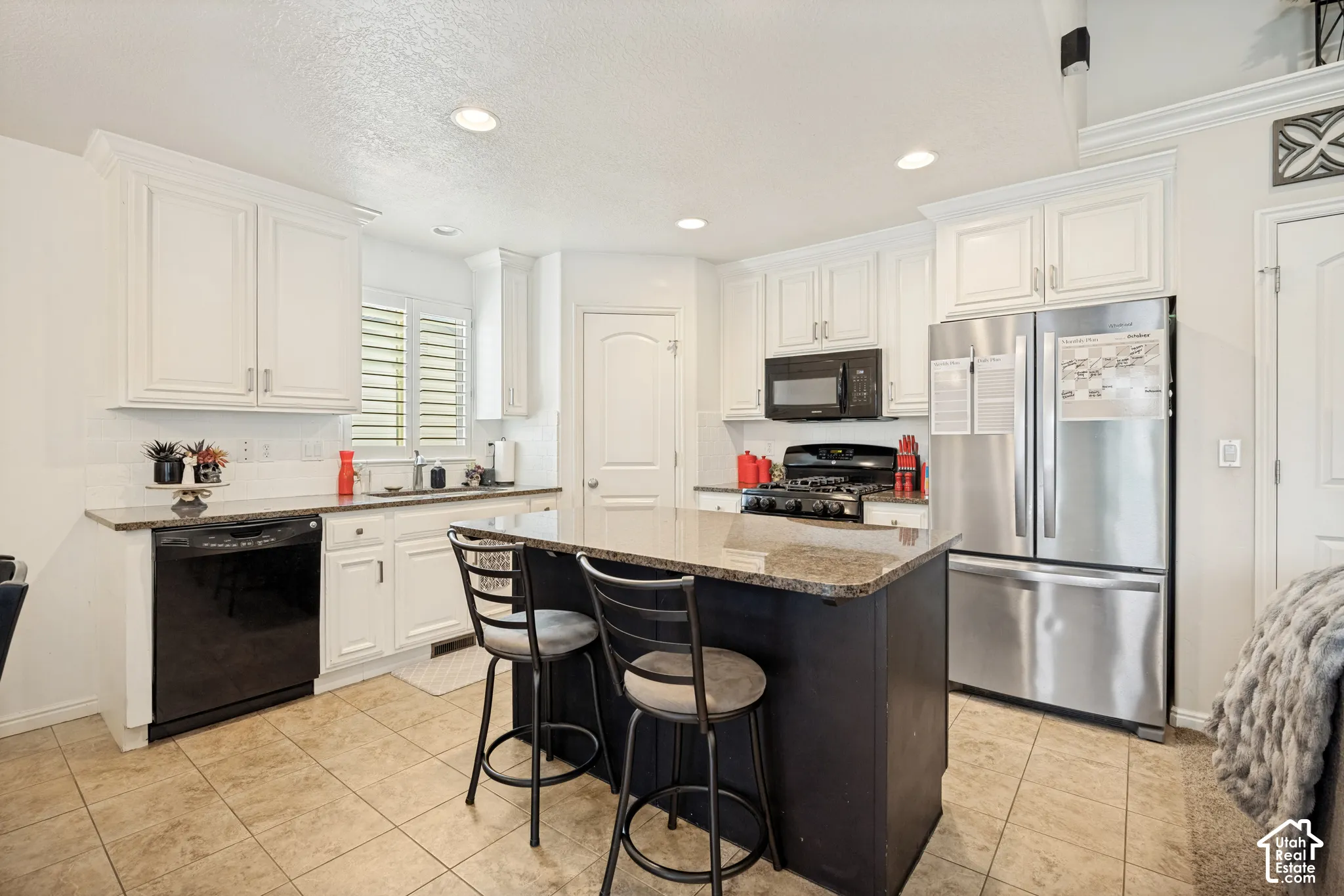 Kitchen featuring white cabinetry, stone-finish countertops, stainless steel appliances, a central island, and ceramic tile flooring