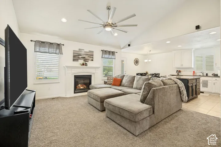Vaulted ceilings featuring a multi-blade ceiling fan, inset lighting, a fireplace with a white mantel, and plantation shutters