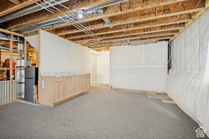 Unfinished lower level featuring exposed wood joist ceilings, wall-to-wall carpeting, and a built-in cabinetry unit with a stone-finish countertop